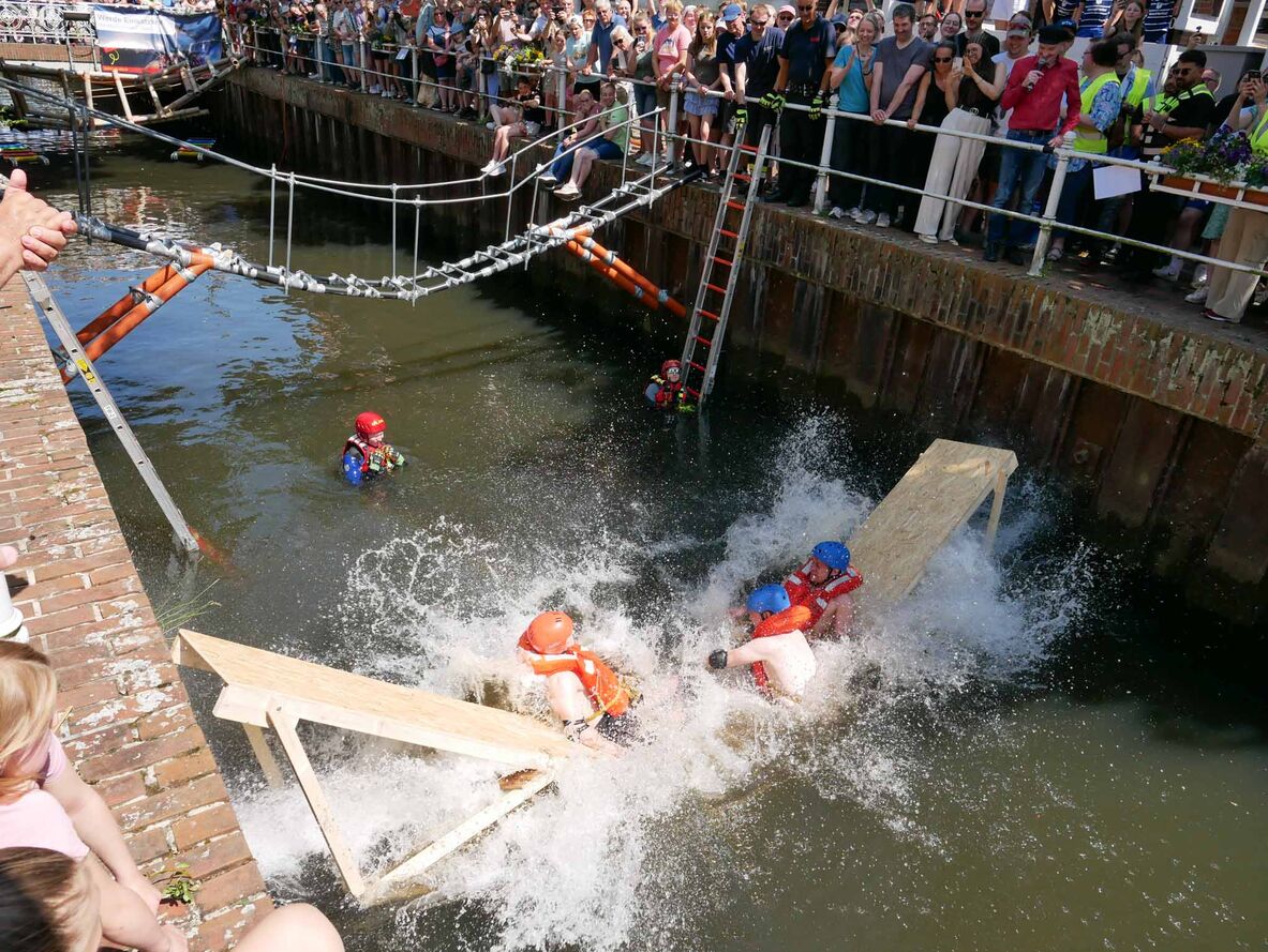 Studierende sind mit ihrer Brücke zusammengebrochen und fallen gerade ins Wasser, das sehr hochspritzt.