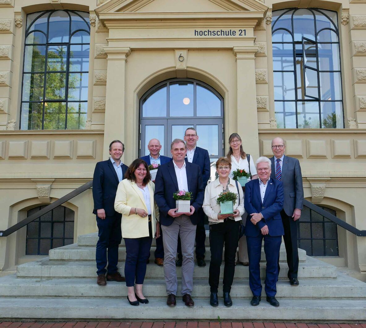 Vertreterinnen und Vertreter der Stiftungen und Fördereinrichtungen stehen mit Blumen in den Händen gemeinsam mit der Hochschulleitung vor dem Hochschulgebäude auf der Eingangstreppe.