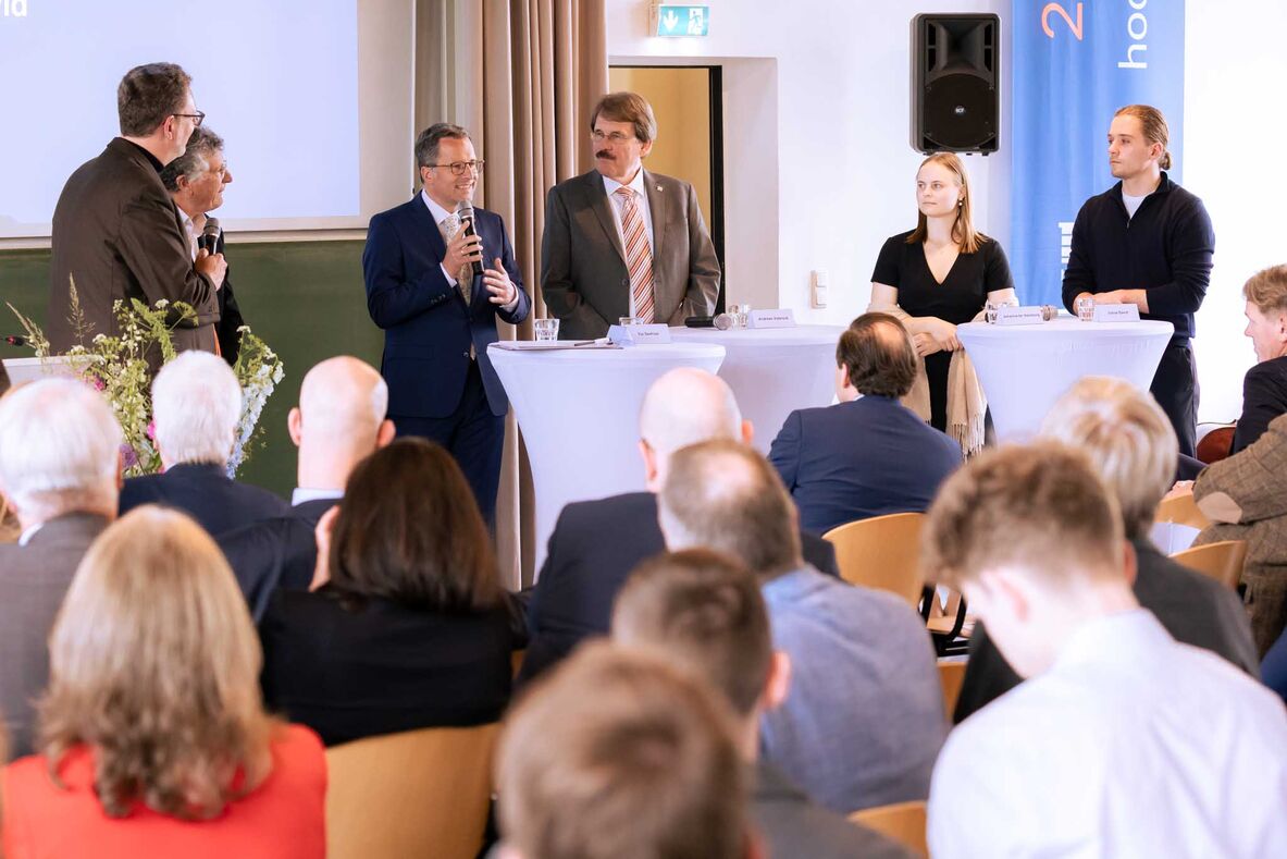 Die Teilnehmenden der Diskussionsrunde stehen an Stehtischen vor dem Publikum.