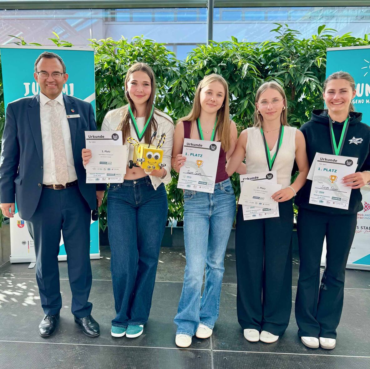 Der Erste Kreisrat Thorsten Heinze steht links neben den vier Mädchen aus dem Siegerteam. Ein Mädchen hält den wie eine Biene aussehenden Roboter in der Hand.