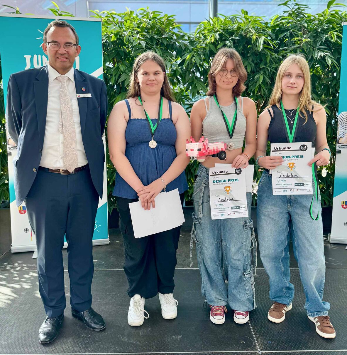 Der Erste Kreisrat Thorsten Heinze steht links neben den drei Mädchen, die den Designpreis für ihren Axolotl-Roboter gewonnen haben.