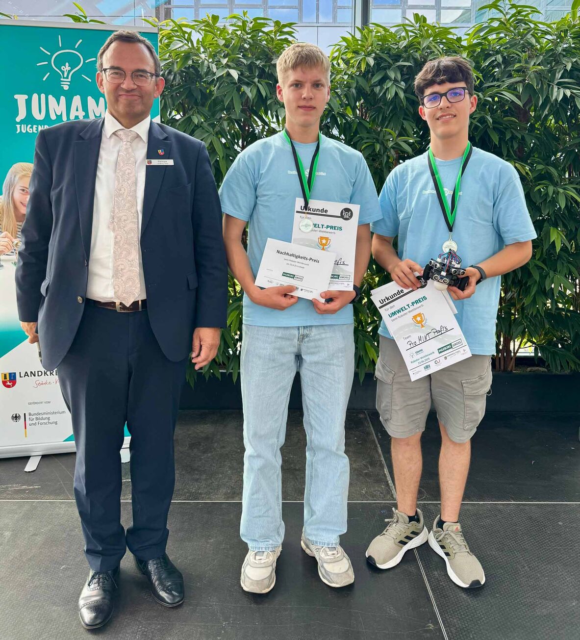 Der Erste Kreisrat Thorsten Heinze steht links neben den beiden Jungen, die für ihren Roboter den Umweltpreis gewonnen haben.