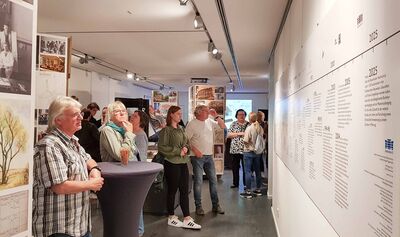 Der Ausstellungsraum mit dem Zeitstrahl rechts an der Wand, der von Besuchern betrachtet wird.