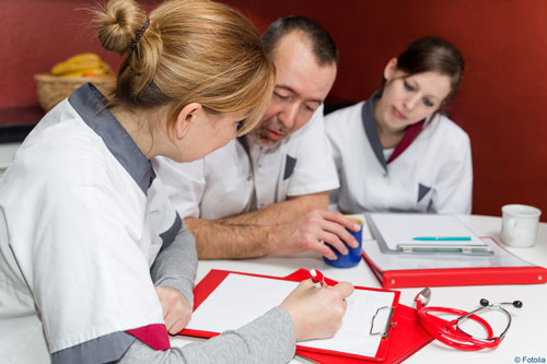 Zwei weibliche Pflegefachkräfte und eine männliche sitzen an einem Tisch und arbeiten an einem Klemmbrett